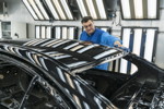 Ein Mitarbeiter prüft die Qualität einer lackierten Karosserie im Decklack-Finish der Lackiererei, BMW Group Werk München 