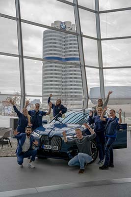 BMW Group Mitarbeitende jubelnd um BMW iX vor BMW Vierzylinder
